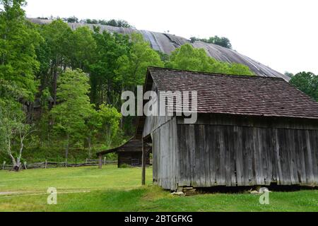 A barn from the historic Hutchinson Homestead is towered over by the signature granite dome of Stone Mountain State Park in North Carolina. Stock Photo