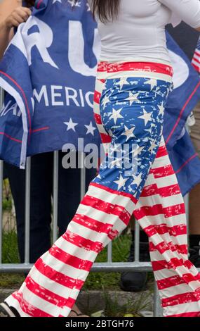 Baltimore, Maryland, USA. 25th May, 2020. Waist-down view of woman in American flag-design pants as she strides by individual behind barricade holding rumpled pro-Trump banner, outside historic Fort McHenry in Baltimore, Maryland; where President Donald Trump and First Lady Melania Trump visit on Memorial Day 2020 despite urging from Baltimore Mayor Bernard C. “Jack” Young to cancel to avoid setting a bad example while the city remains under a stay-at-home order (with exemptions, including some outdoor exercise). Kay Howell/Alamy Live News Stock Photo