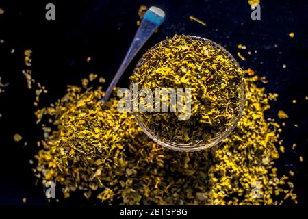 Close up short of popular Indian Spice Kasuri Methi (Dried Fenugreek Leaves) in a bowl and some on a spoon on a black colored glossy surface. Stock Photo