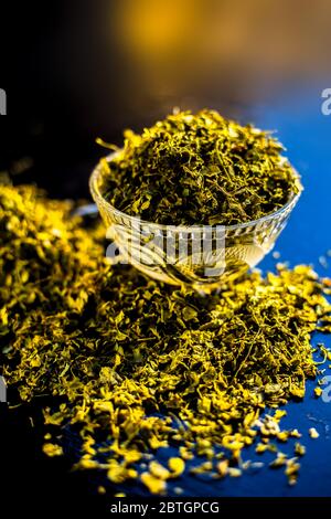 Close up short of popular Indian Spice Kasuri Methi (Dried Fenugreek Leaves) in a bowl and some on a spoon on a black colored glossy surface. Stock Photo