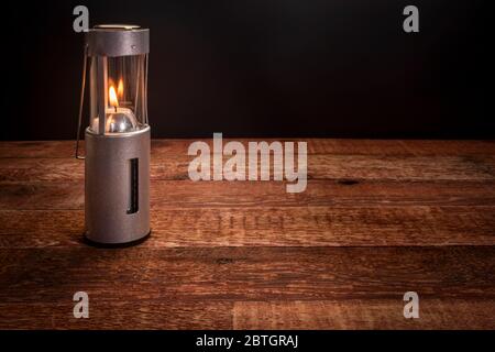 collapsible camping candle lantern burning in darkness on a rustic