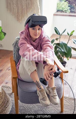 Fashion teen girl wear vr headset look at camera sit in chair, vertical portrait. Stock Photo