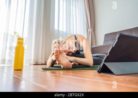 Fitness woman exercising on the floor at home and watching fitness videos in a tablet. People do sports online because of the coronovirus Stock Photo