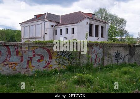 An old mansion, now closed, decaying and rotting, next to a graffiti covered brick fence, wall. The area is waiting for redevelopment. In Vilnius, Lit Stock Photo