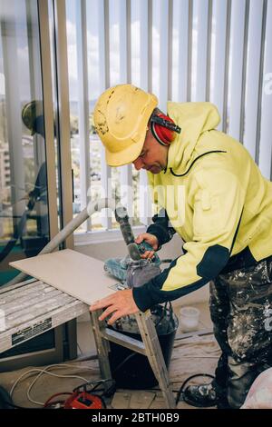 Master cuts the tile using an angle grinder with special diamond disc. Concept renovation repair, overhaul, contract tiler. Stock Photo