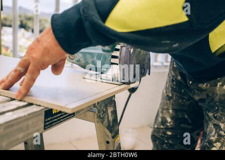 Master cuts the tile using an angle grinder with special diamond disc. Concept renovation repair, overhaul, contract tiler. Stock Photo