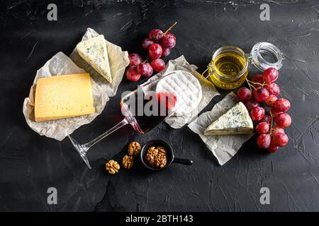 Grapes, red wine, cheeses, brie cheese , blue, chease honey and nuts over black background top view. Stock Photo