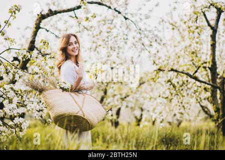 Beautiful young woman with wicker bag in spring apple blossom. Stock Photo