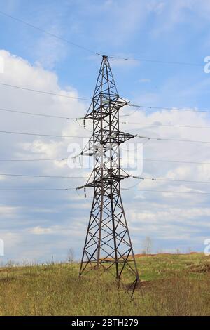 Iron pylon of a high voltage power line stands in a field against a blue sky. Stock Photo