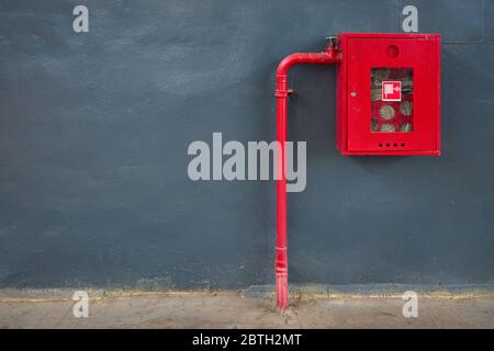 Fire hose in red box, pipe roll for fire emergency in red metal cabinet on gray painted concrete wall with tiled floor as part of firefighting system Stock Photo