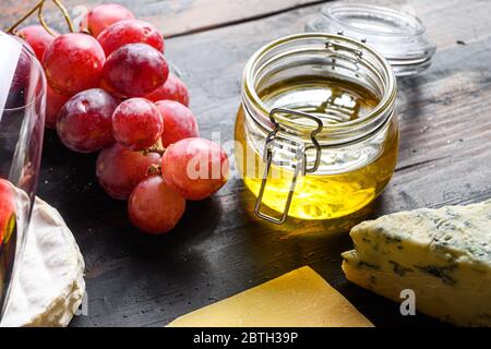 Honey in jar selective focus grape and french mold cheese close up. Stock Photo