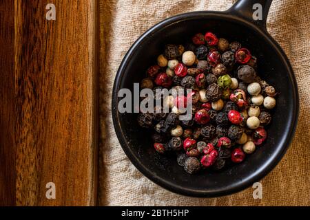 Ground Black, white and pink rose peppers in bowl assorted and spicy on linen rustic kitchen cloth, copy space, top view Stock Photo