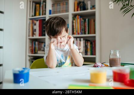 Tired child upholding his head with arm. Boy getting sleep after doing school assignments. Stock Photo