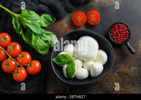 Mozzarella cheese, cherry tomatoes and basil leaves rose pepper on a dark rustic metal background, Italian cuisine ingredients for caprese salad top v Stock Photo