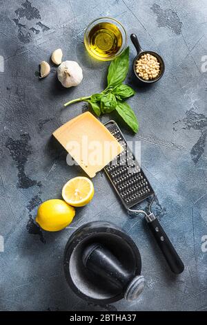 Pesto genovese sauce Ingredients italian recipe Fresh basil, tomatoes mortar lemon olive oil parmesan pine nuts on the stone table on gray concrete ba Stock Photo