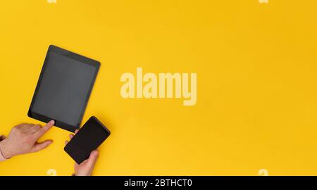 Closeup at man hands hanging cellphone and tablet on yellow background,  Stock Photo
