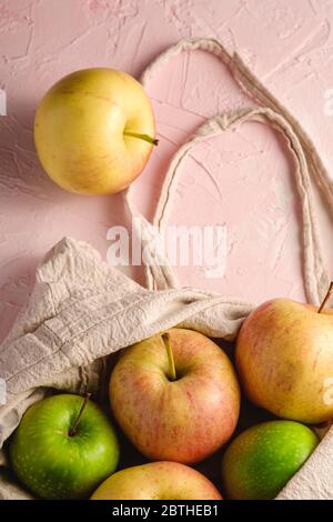 Fresh sweet apples in reusable textile grocery bag on pink textured background, selective focus Stock Photo