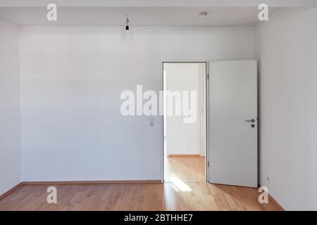 Open door and white wall in empty room with hardwood parquet at home Stock Photo