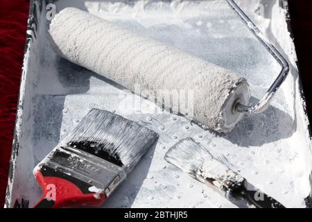A roller and paint brushes in a paint tray. The are used to apply paint onto walls during home improvement. Stock Photo