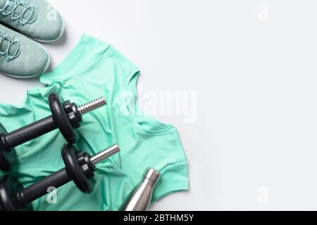 Sport and fitness equipment, female tee-shirt, black dumbbells, shoes, water bottle on grey. View from above, space for your text. Stock Photo