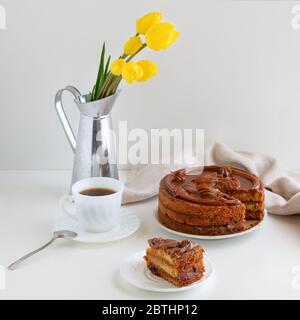Homemade cake, two cups of coffee and tulips in a vase against a light background. Home baking concept. Square format. Stock Photo