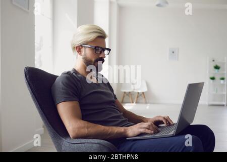 Work online. Smart young man freelancer using laptop in living room. Stock Photo