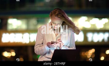 Young beautiful female using smartphone sitting with laptop outs Stock Photo