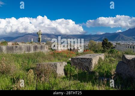 Landscape with the ruins of Pompeii in Italy, red poppies, mountains, blue sky, white clouds. The bronze sculpture Daedalus by Igor Mitoraj Stock Photo