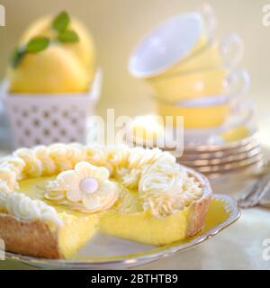 Closeup of yummy lemon tart with juicy filling and creative cream decoration put on porcelain plate near tea set and lemons, shot for copy space Stock Photo