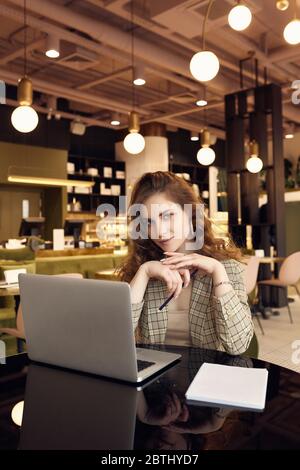 Portrait of confident young businesswoman in smart casual wear makes notes in a notebook in a coffee shop interior Stock Photo