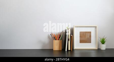 Stationary in wooden pencil holder putting on wooden working desk that surrounded by books, notebook, empty picture frame and potted plant over sittin Stock Photo
