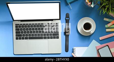 Top view image of computer laptop with white blank screen putting on colorful working desk surrounded by smart watch, coffee cup, notebook, smartphone Stock Photo