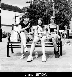 Mother And Daughters Sitting On A Bench In South London During The Coronavirus Lockdown While Out Shopping Stock Photo