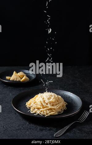 Cacio e Pepe - Italian Pasta with Cheese and Pepper. Spaghetti Sprinkled Cheese on Black Plate on Dark Background. Stock Photo