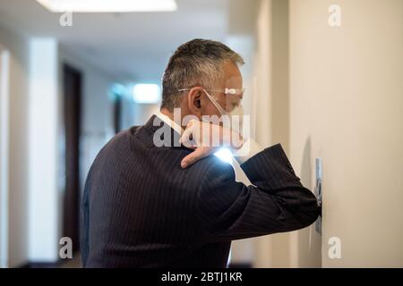 Mature Japanese businessman with mask and face shield pressing elevator button with elbow Stock Photo