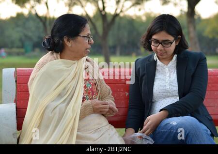 Shot of a senior retired Indian woman sitting in a park with her daughter in law on a red bench peeling peanuts, and eating them. Concept - Happy Reti Stock Photo