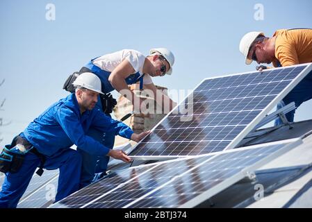 Male team engineers installing stand-alone solar photovoltaic panel system. Electricians mounting blue solar module on roof of modern house. Alternative energy concept. Stock Photo