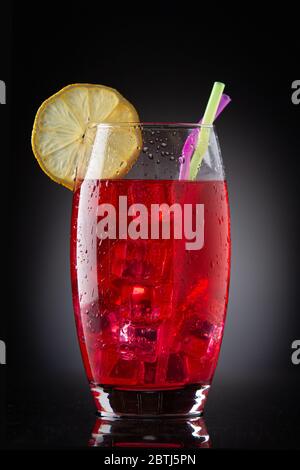 glass with red drink with ice, straws and lemon on black background Stock Photo
