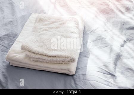 White clean towels on the bed with grey bedlinen. Stock Photo