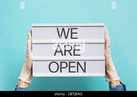 Woman's hands in gloves holding plate with text We Are Open. Stock Photo
