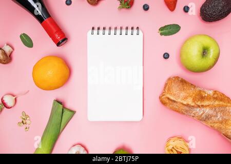 Different groceries: bread, wine, fruits,vegetables on pink background and empty notepad. Stock Photo