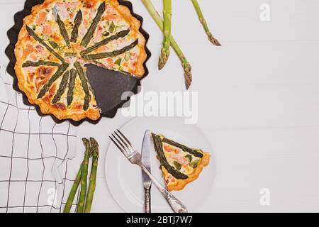 Tart or quiche with green asparagus and salmon on white wooden table Stock Photo