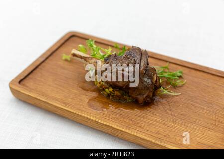 roasted meatshank baked whole lies with fresh tomato greens and hot pepper on a platter on an old wooden surface Stock Photo