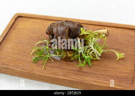 roasted meatshank baked whole lies with fresh tomato greens and hot pepper on a platter on an old wooden surface Stock Photo