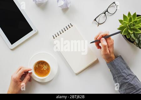 Man working writing in the notepad and drinking coffee at his workplace Stock Photo