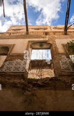 First floor of abandoned house, view from inside through a broken ceiling. Broken traditional tiles on the walls between door and windows. Blue sky wi Stock Photo