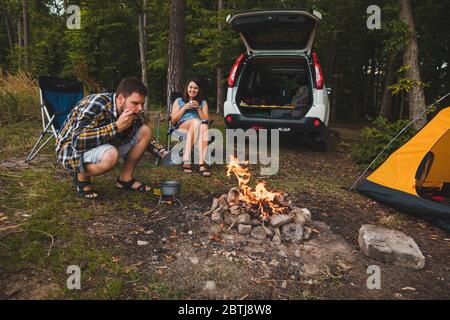 couple sitting near campfire. man cooking on fire. hiking concept Stock Photo