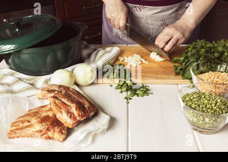 Cooking of dried split pea soup with pok ribs. Woman cuts onions and herbs. Stock Photo