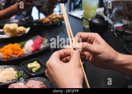 Hand using chopsticks pick Sushi and Sashimi rolls. Fresh made Sushi set with salmon, prawns, wasabi and ginger. Traditional Japanese cuisine. Stock Photo