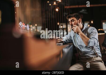 Young man drinking beer, smoking cigarette and using mobile phone at the pub Stock Photo